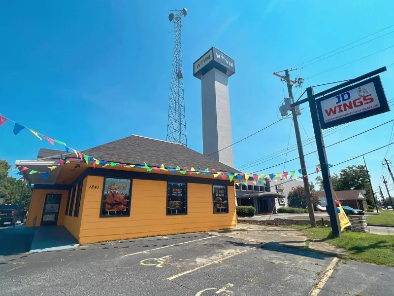 The exterior of JD WINGS with bright yellow walls and colorful flags at JD WINGS, an Fast food Restaurant in Columbus